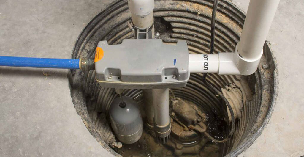 Pompe à puisard installée dans une cuve de collecte au sous-sol d'une maison résidentielle à Montréal, tuyau de refoulement visible